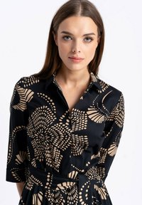 Sukienka zapinana na guziki z czarnym tłem i beżowym kwiatowym wzorem, z kołnierzykiem, rękawami 3/4 i wiązaniem w talii.