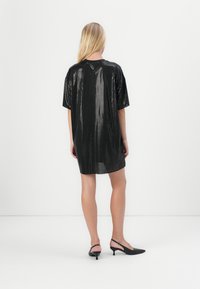 Crna haljina sa sequinom, oversized kroja i kratkim rukavima, labavog kroja, glatke teksture i suptilnog sjaja, u kombinaciji s crnim slingback potpeticama.