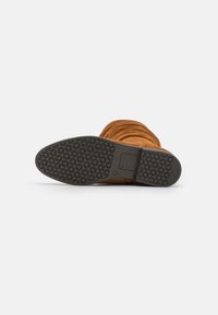 Bottine en daim marron avec une texture plissée, dotée d'une semelle en caoutchouc noir avec un profil sculpté pour une meilleure traction.