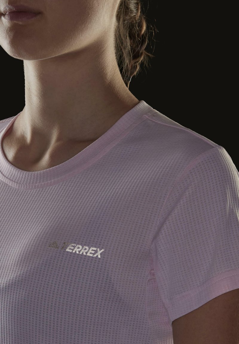 Hellrosa Sportoberteil mit kurzen Ärmeln aus strukturiertem Stoff. Verfügt über einen Rundhalsausschnitt und ein reflektierendes "TERREX"-Logo auf der Brust.