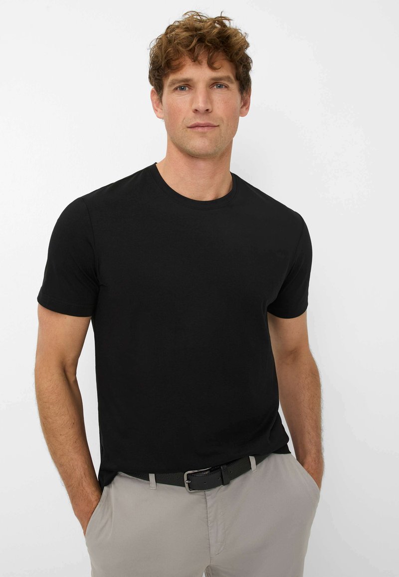 Zwart T-shirt met ronde hals van katoen, met korte mouwen. Gecombineerd met lichtgrijze broek en een zwarte riem, gedragen door een mannelijke model.