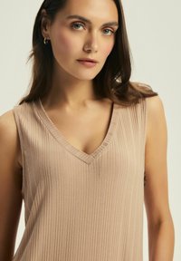 Beżowy prążkowany top bez rękawów z dekoltem w kształcie litery V, z pionowymi paskami i miękką teksturą. Minimalistyczny design, bez widocznych wzorów czy akcentów.