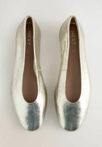 Metallisch goldene Ballerinas mit einer glatten, glänzenden Textur, runder Zehenpartie und niedrigem Schnitt. Logo innen im Schuh sichtbar.