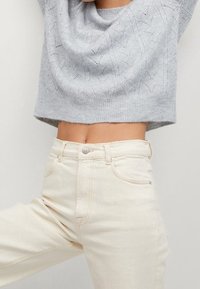 Hellgrauer, gestrickter Cropped-Pullover mit einem strukturierten Muster, kombiniert mit hochgeschnittenen, cremefarbenen Denim-Jeans mit Fronttaschen.