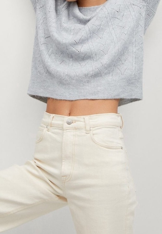 Hellgrauer, gestrickter Cropped-Pullover mit einem strukturierten Muster, kombiniert mit hochgeschnittenen, cremefarbenen Denim-Jeans mit Fronttaschen.