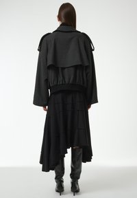 Zwarte gelaagde jurk met streepjes, vergezeld van een cropped zwarte jas met een uitlopende achterkant en geribbelde zoom, in combinatie met kniehoge zwarte laarzen.