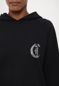 Felpa nera con tasca frontale. Presenta un logo in strass argento sul petto sinistro. Tessuto morbido con una vestibilità comoda e cappuccio.