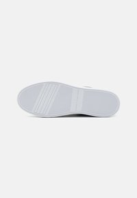 Suola di sneaker in gomma bianca con un motivo di grip testurizzato e un marchio discreto. Forma liscia e arrotondata con bordi dritti e linee di battistrada definite.