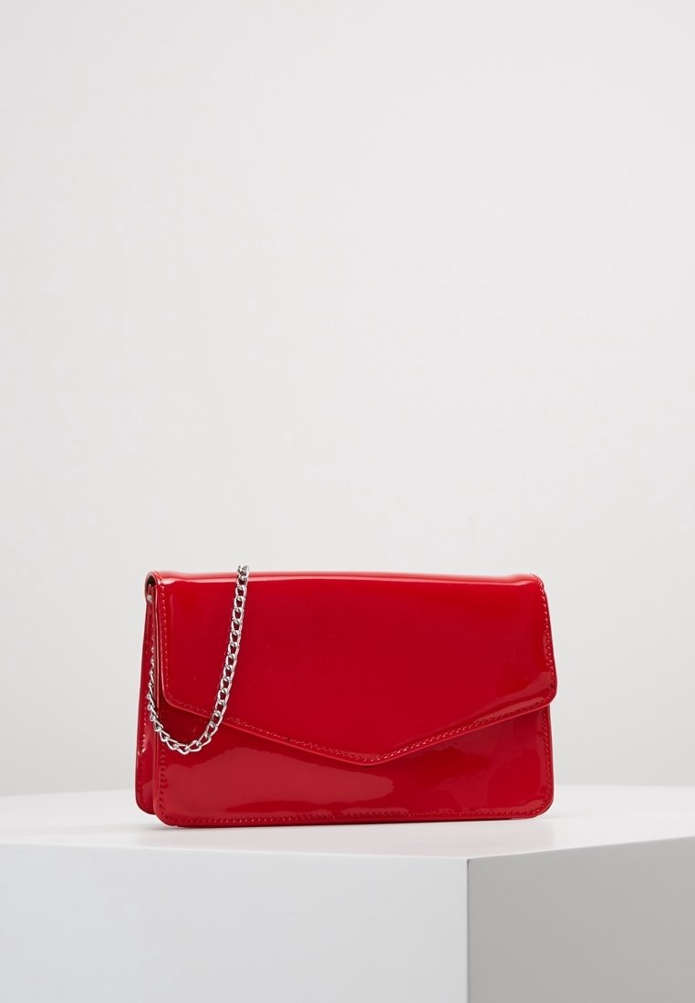 Pochette rouge brillante rectangulaire avec une chaîne argentée reposant sur une surface blanche sur un fond uni.