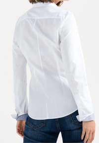 Bílá košile s dlouhými rukávy a přiléhavým střihem, která má kontrastní modrý vzorovaný manžet a jemné záhyby na zadní straně pro lepší tvar.