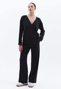 Top avvolgente nero con maniche lunghe e un nastro, abbinato a pantaloni neri a gamba larga. Il tessuto morbido e il design a scollo a V creano una silhouette elegante.
