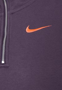 Fialová mikina na zip z texturované látky, s oranžovým vyšívaným logem Nike na levé straně a kovovým zipem.