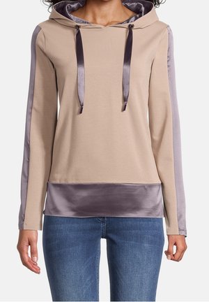 Sweat à capuche beige avec des panneaux en satin violet sur les manches et l'ourlet, cordons en satin, porté avec un jean bleu.