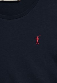 Kortärmad marinblå t-shirt i bomull med en liten röd broderad figur som svingar en klubba, rund halsringning och mjuk yta.