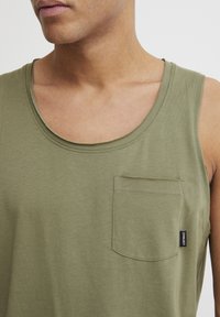 Olivgrünes Tanktop aus weichem Material. Mit rundem Ausschnitt, einer Brusttasche und einem Markenlabel an der Seitennaht.