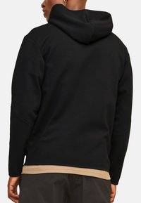 Zwarte hoodie met een zachte textuur, voorzien van een kangoeroezak en een contrasterende beige zoom, ontworpen voor comfort en warmte.