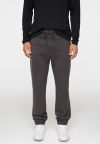 Szare spodnie dresowe z elastycznym pasem z troczkiem, elastycznymi mankietami i gładką fakturą, w zestawie z czarną koszulą z długim rękawem oraz białymi sneakersami.