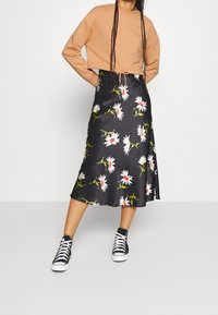 Klar beige sweatshirt med långa ärmar, matchad med en svart blommig midiklänning prydd med vita tusenskönor och röda mittpunkter, bärs med svarta sneakers.