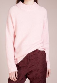 Ljust rosa, fluffig tröja med hög ribbad krage och ribbade ärmar, parat med mörk burgundy byxor med ett blommönster.