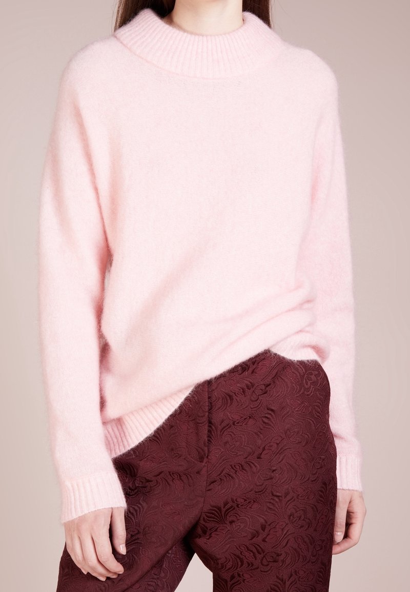 Ljust rosa, fluffig tröja med hög ribbad krage och ribbade ärmar, parat med mörk burgundy byxor med ett blommönster.