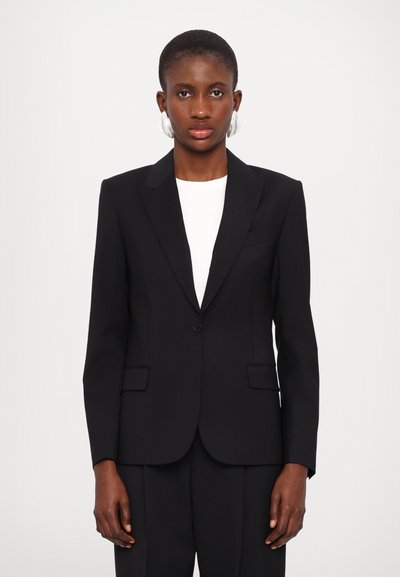Zwart op maat gemaakte blazer met schouderclappen, enkele knoopsluiting en twee voorzakken. Gemaakt om te dragen over een witte top en geschikt voor formele gelegenheden.