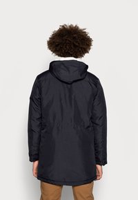 Mörk marinblå parka-jacka med huva, som har en mjuk fleecefoder och en rak passform. Tyget verkar slätt och vattenavvisande.