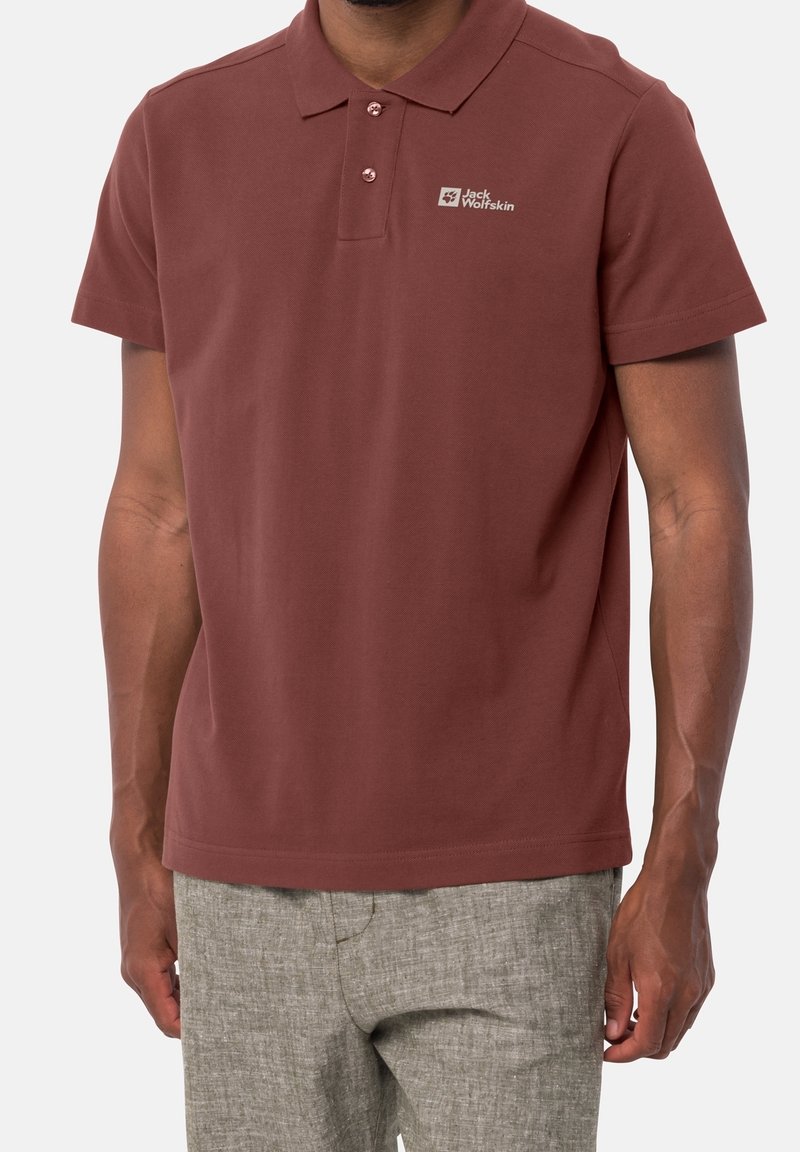 Polo bordeaux à col avec patte à trois boutons et logo brodé. Texture douce et lisse, associé à un pantalon gris clair.