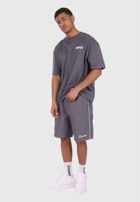 Grå bomulds t-shirt og matchende shorts med hvide logo detaljer. Skoene er hvide sneakers med branding, hvilket fuldender det koordinerede outfit.