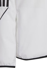 Witte sportjack met een gladde textuur, zwarte accenten aan de onderrand en drie verticale zwarte strepen aan de bovenlinkerzijde.