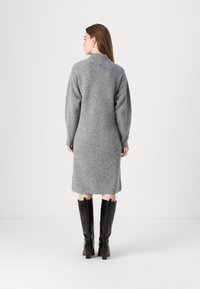 Grau, geripptes Strickkleid mit langen Ärmeln und hohem Halsausschnitt, kombiniert mit kniehohen, schwarzen, glänzenden Stiefeln. Glatte Textur und figurbetonter Schnitt.