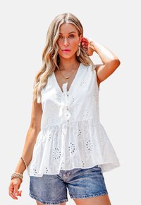 Witte, geborduurde katoenen peplumblouse met een V-hals, strikdetail en bloemvormige uitsparingen, gecombineerd met denim shorts. Geweven, lichtgewicht stof.