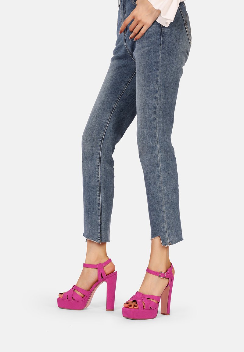 Sandali con piattaforma fucsia e tacco alto, con cinturini incrociati; texture scamosciata; tacco grosso; design open-toe; abbinati a jeans azzurri chiari.