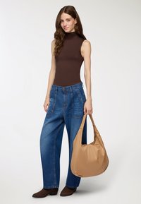 Brązowy bezrękawnik z golfem, niebieskie szerokie dżinsy z przednimi kieszeniami oraz jasnobeżowa torba na ramię z miękkiego materiału. Brązowe botki na obcasie.