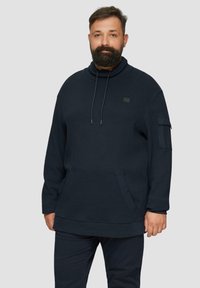 Sweat à capuche oversized bleu marine avec un col montant, doté de cordons de serrage ajustables, d'une poche avant et d'une poche sur la manche. Tissu doux et texturé.