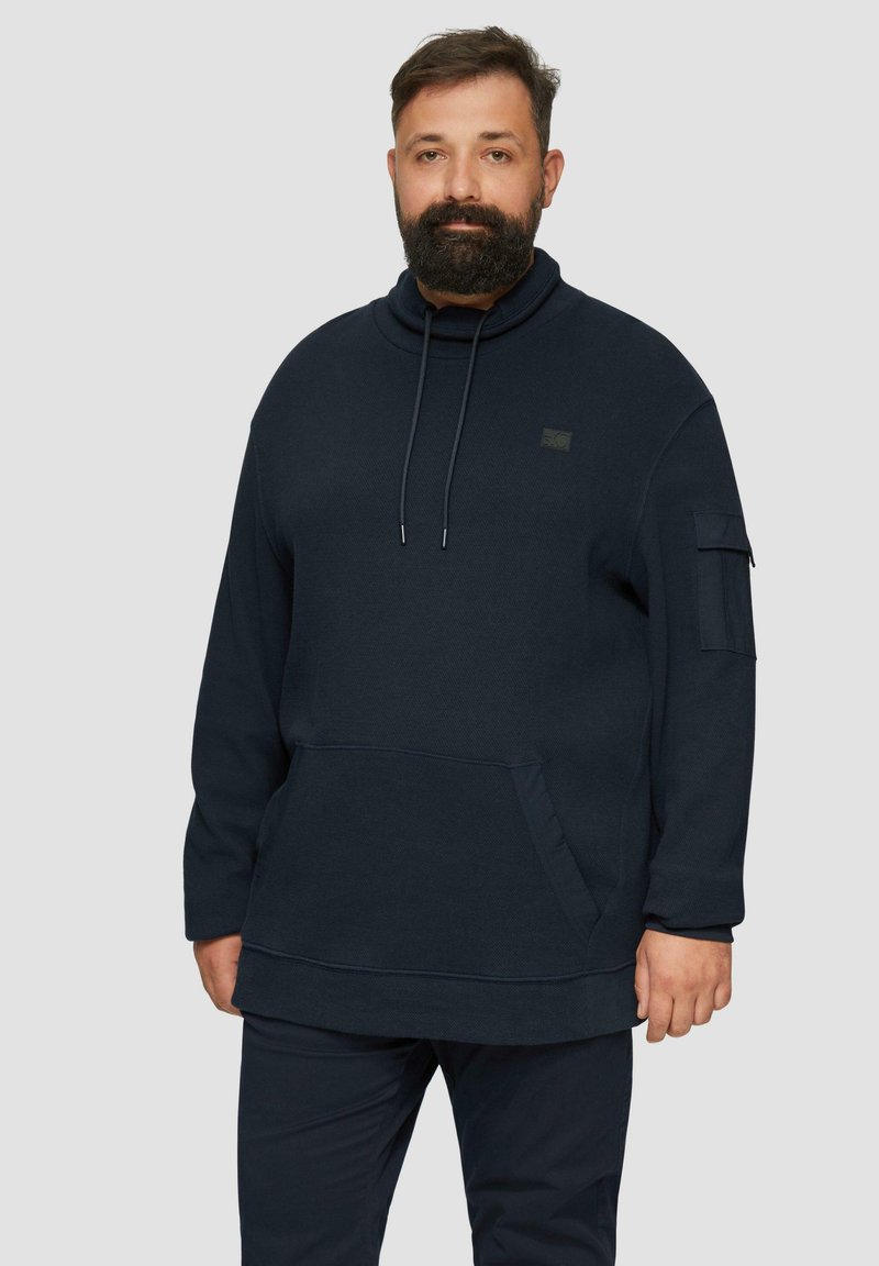 Sweat à capuche oversized bleu marine avec un col montant, doté de cordons de serrage ajustables, d'une poche avant et d'une poche sur la manche. Tissu doux et texturé.
