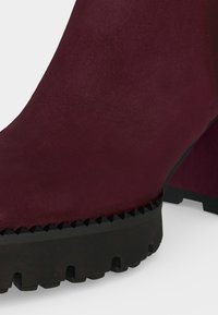 Gros plan d'une botte en daim bordeaux avec une semelle en caoutchouc noire épaisse dotée de crampons profonds pour l'adhérence et un talon bloc.