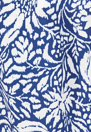 Motif de feuilles tropicales blanches et florales sur tissu bleu avec de légers plis créant des ombres douces et de la texture.