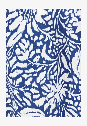Motif de feuilles tropicales blanches et florales sur tissu bleu avec de légers plis créant des ombres douces et de la texture.