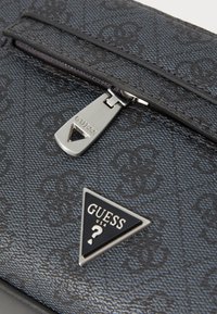 Schwarze, gemusterte synthetische Handtasche mit einem Reißverschlussverschluss, einer silbernen Hardware-Tag und einem dreieckigen Markenlogo auf der Vorderseite.