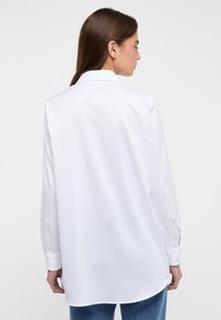 White long-sleeve shirt made of smooth cotton fabric, featuring a classic collar and button detail at the cuff, slightly curved hem.