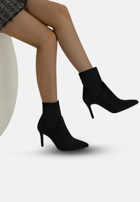 Gambe di donna incrociate, che indossa stivaletti neri con tacco a spillo e polsini a coste simili a calze.