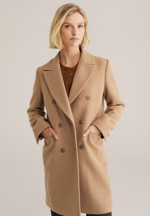 Cappotto doppiopetto color tan realizzato in morbida lana, con grandi bottoni, rever a punta e tasche laterali, dal taglio rilassato.