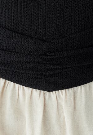 Černý texturovaný top s nařasením, spárovaný s světle krémovou skládací sukní, vytvářející kontrast v barvě a struktuře látky.