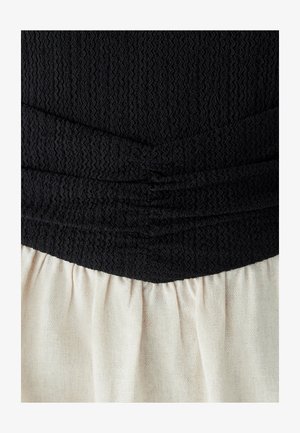 Černý texturovaný top s nařasením, spárovaný s světle krémovou skládací sukní, vytvářející kontrast v barvě a struktuře látky.