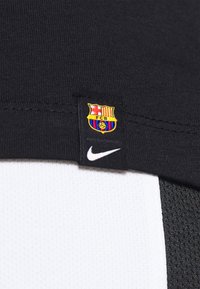 Černá látková visačka s erbem FC Barcelona a bílým logem Nike, přišitá na černobílém sportovním materiálu.