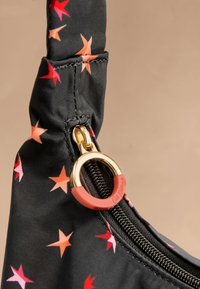 Borsa in tessuto nero con motivi di stelle rosse e rosa. I dettagli includono una cerniera dorata con un accento rosso e una chiusura a zip.