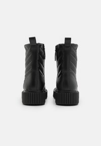 Stivali ankle neri impermeabili con texture trapuntata, dotati di zip laterale, linguetta e suola in gomma spessa con un motivo rigato.