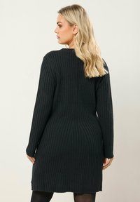 Abito in maglia nero con texture a coste, maniche lunghe e orlo leggermente svasato. Presenta un collo rotondo e una silhouette aderente.