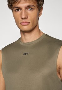 Olivgrünes ärmelloses Sportshirt mit glatter Textur, das ein schwarzes Logo auf der oberen linken Seite und einen runden Ausschnitt aufweist.