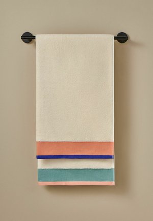 Toalla beige con bloques de color coral, azul y verde colgada en una barra negra de toallas montada en la pared contra una pared beige.